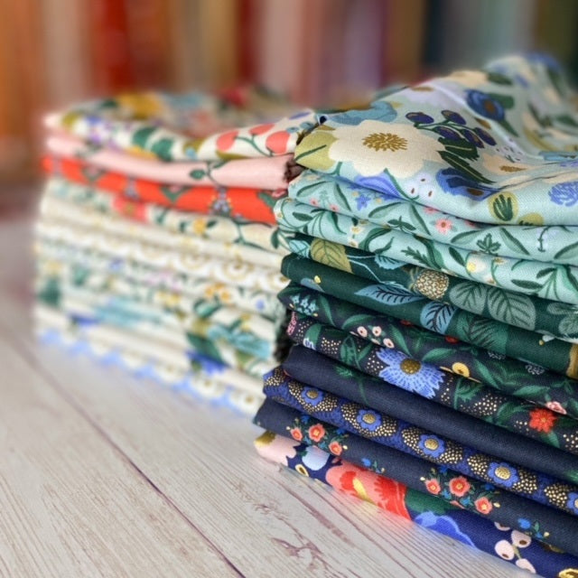 fat quarters of rifle paper company florals are folded into two stacks.  In front are blues and greens and at the back are cream pink and red fabrics